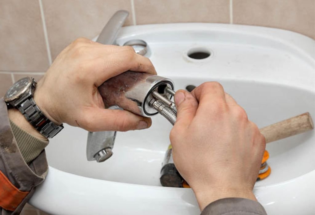 Professional technician in Dallas installing a chrome P-trap and drainage pipe under a bathroom sink using a wrench.